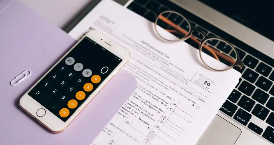 A smartphone with a calculator app on tax documents next to a laptop, emphasizing modern accounting.