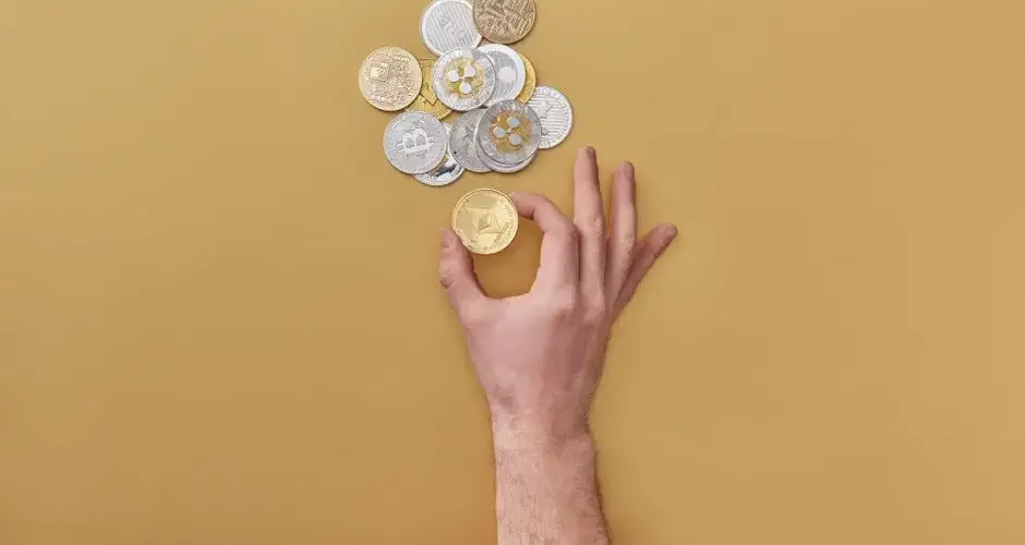 Hand holding coins with various cryptocurrencies on a yellow background. Perfect for finance-themed designs.