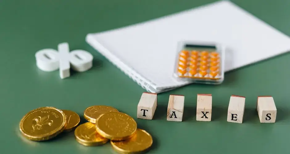 Close-up of tax-related items including coins, calculator, and word 'taxes' on a green background.