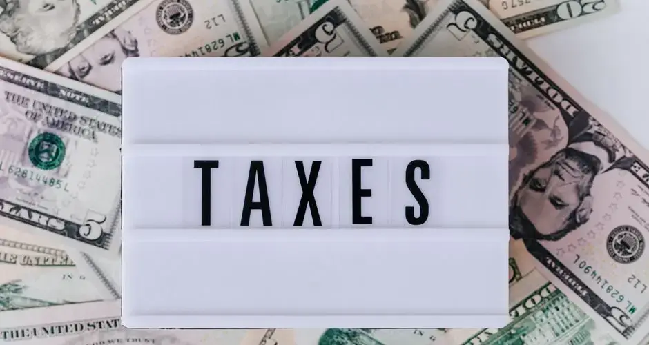 Top view of white vintage light box with TAXES inscription placed on stack of USA dollar bills on white surface