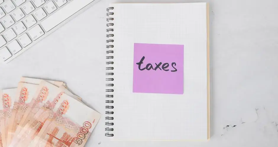 Flat lay image of tax preparation, featuring cash, a notebook, and a computer keyboard on a white surface.