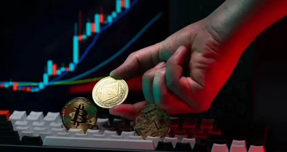 Close-up of a hand holding cryptocurrency coins on keyboard, with a graph display in the background.