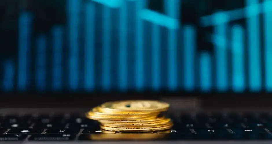 Stack of gold coins on a laptop keyboard with a rising graph, symbolizing financial growth.