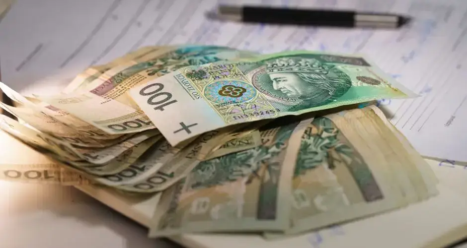 Stack of Polish zloty banknotes on financial documents with a pen, indicating monetary transactions in an office setting.