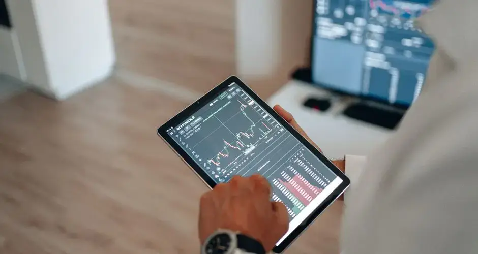 Close-up of hands using a tablet for online trading and market analysis.