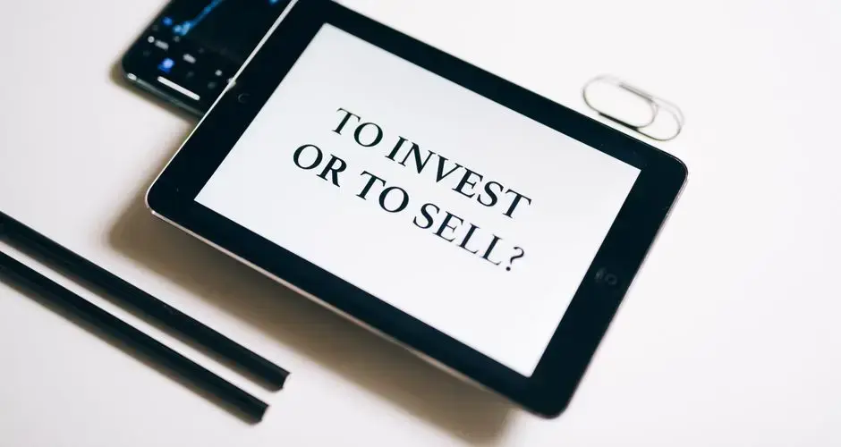 A tablet with text 'To Invest or To Sell?' on a white background.