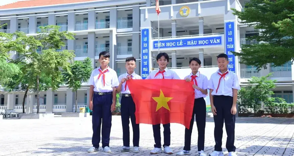 Group of Vietnamese students in school uniform proudly holding national flag in schoolyard.