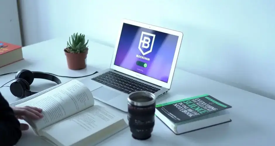 A laptop displaying blockchain technology in a modern workspace with books and headphones.