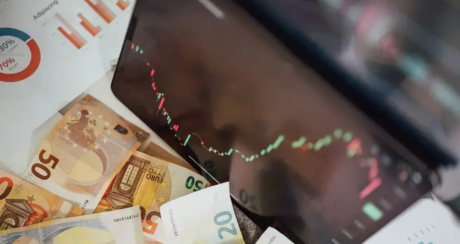 Close-up of euro banknotes with a digital stock market chart displaying a downward trend, symbolizing financial volatility.