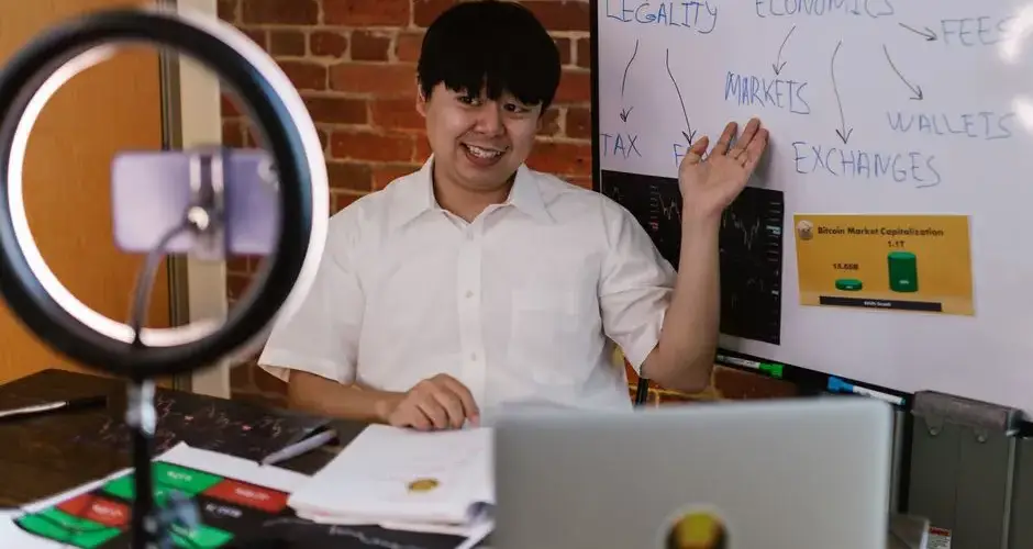 Asian man explaining cryptocurrency market with whiteboard indoors.