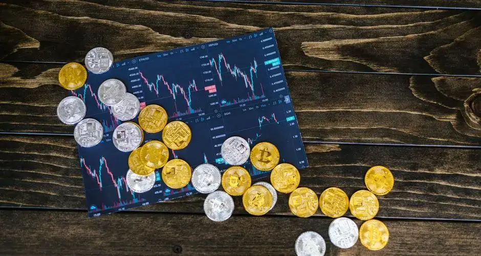 Gold and silver cryptocurrency coins scattered on a trading chart over a wooden table.