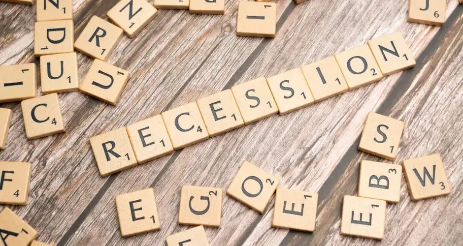 Wooden letter tiles on a wooden surface spell out the word "Recession," symbolizing economic downturn.