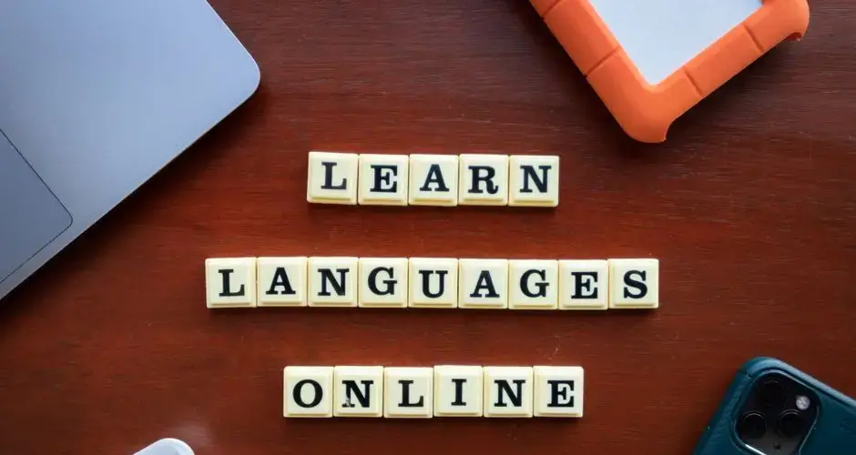 Flat lay of language learning tools with devices and text blocks on desk.