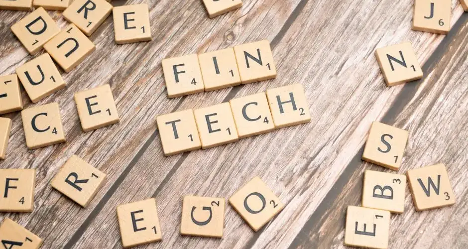 Fintech spelled out with wooden letter tiles on a rustic wooden background.