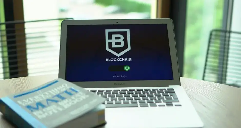 A laptop displays a blockchain screen next to a math textbook, symbolizing digital finance and education.