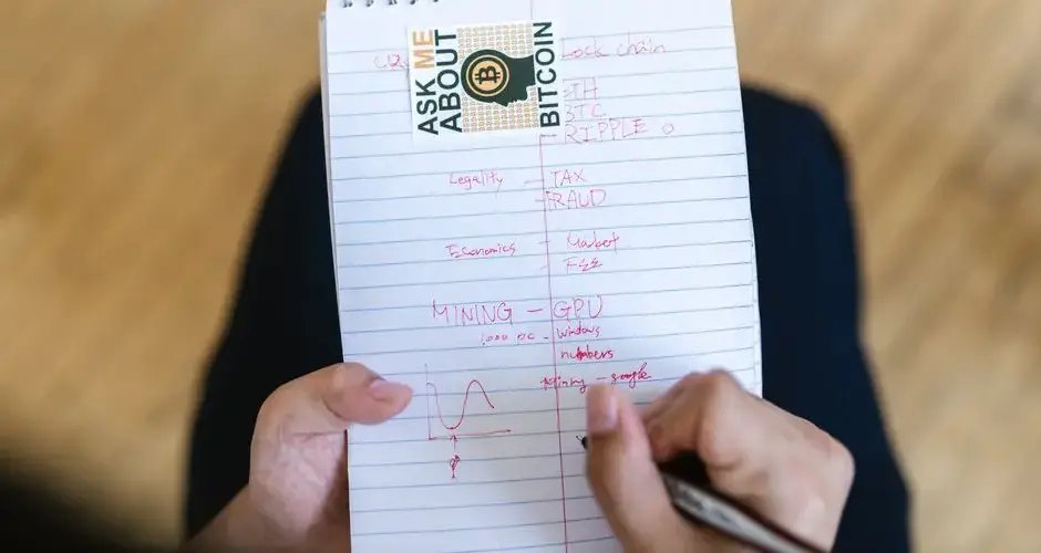 Close-up of a person writing notes about bitcoin and cryptocurrency on a notepad.