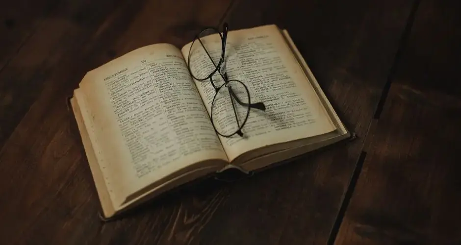 Open vintage book with eyeglasses resting on a wooden surface, evoking a sense of nostalgia.