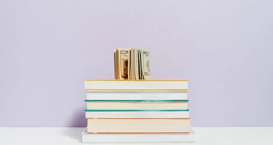 Stack of books with a stack of US dollar bills on top against a pastel background.