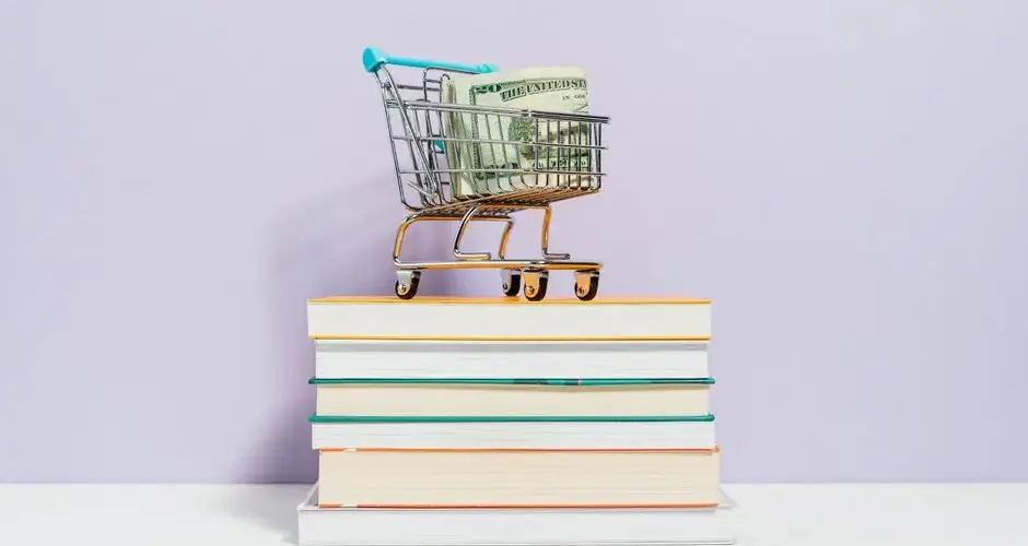A small shopping cart with dollar bills placed on a stack of books, symbolizing financial literacy.