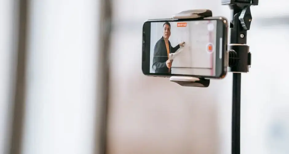 A lecturer conducting an online class using a smartphone mounted on a tripod.