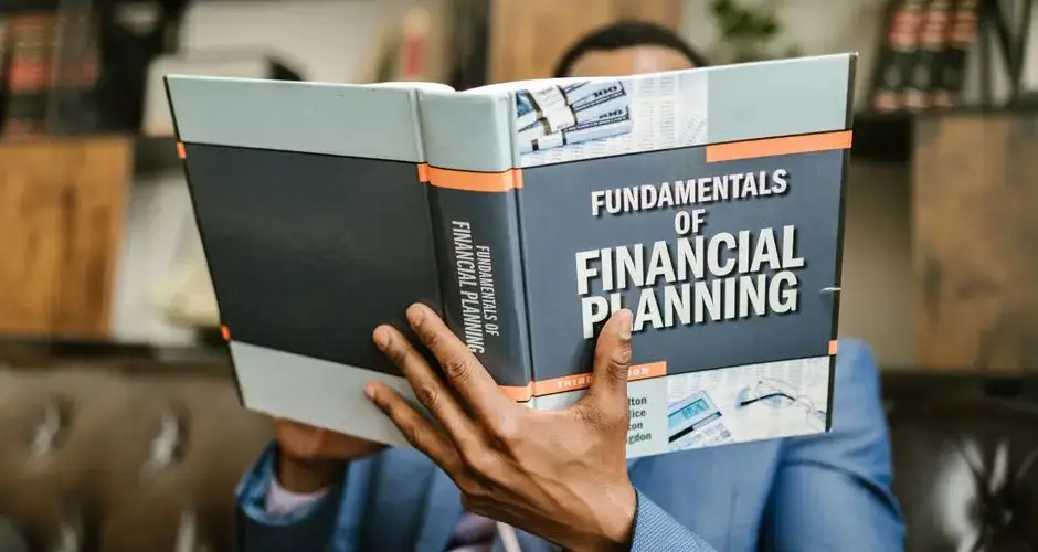 A professional individual in a suit reading 'Fundamentals of Financial Planning' indoors.
