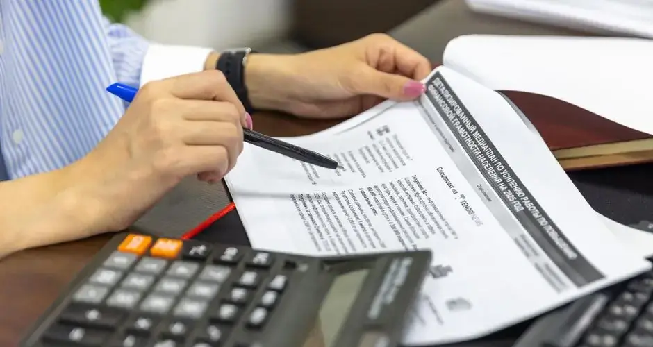 Close-up of a person analyzing financial documents using a calculator and pen.