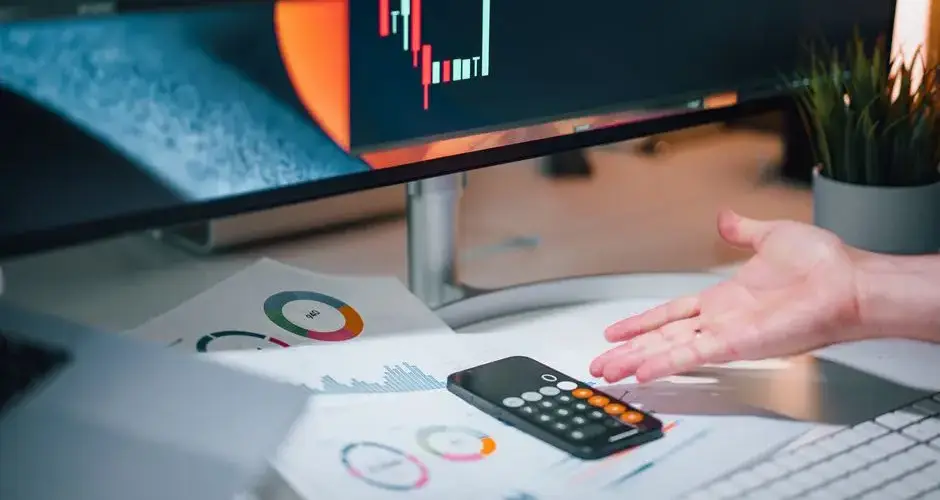 Businessman analyzing stock market data on computer monitor with documents and calculator.