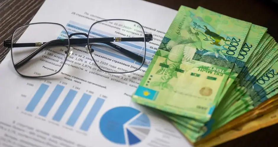 Kazakhstani tenge notes and financial reports on a desk, depicting financial analysis.