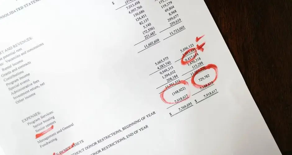 Financial statement with red annotations on a wooden table.
