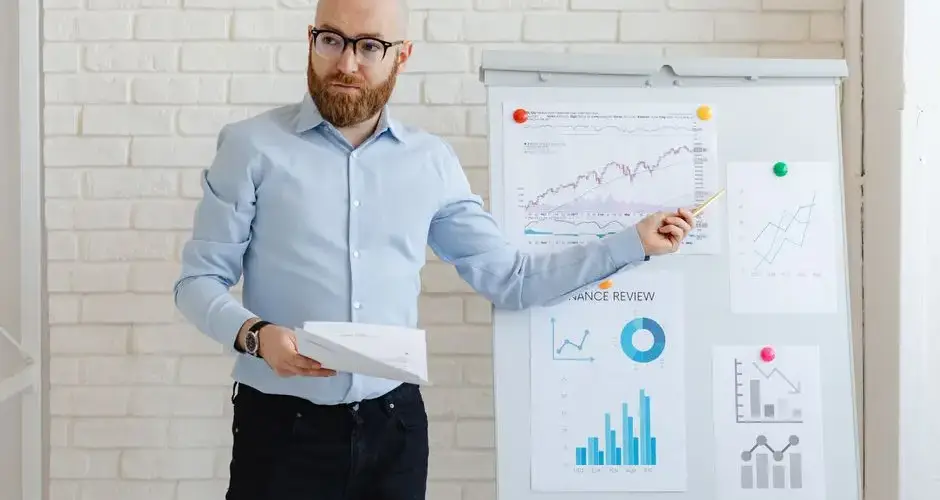 A man presenting financial charts on a whiteboard in an office setting.