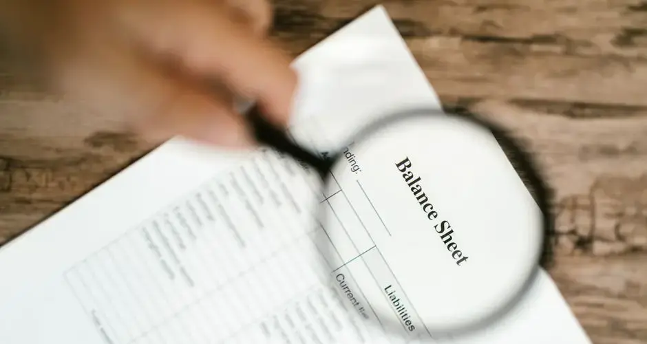 Close-up of a balance sheet under a magnifying glass on a wooden table.