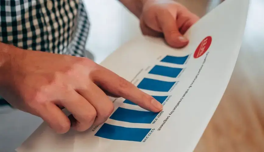 Close-up of hands pointing at a bar chart on paper, analyzing financial stats and report.
