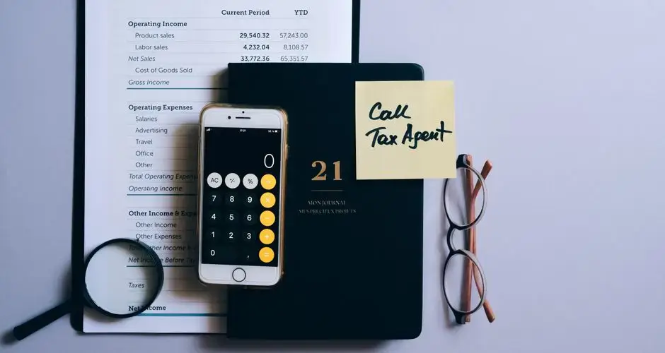 Top view of a desk with income statement, phone calculator, and tax reminder note.