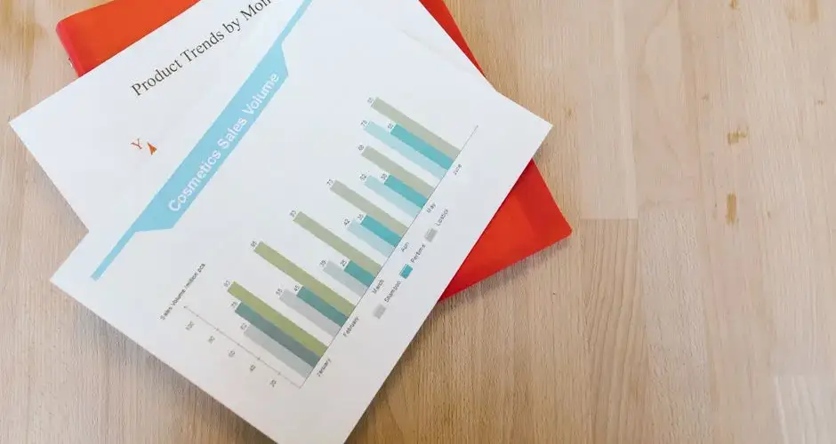 Top view of a cosmetics sales volume report with charts on a wooden desk.