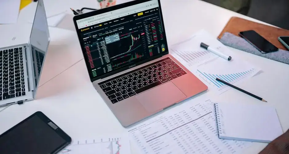 Laptops on a desk displaying stock market charts and financial documents.
