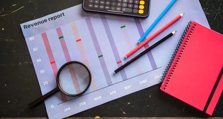 Flat lay of revenue report with a calculator, pencils, and notebook.
