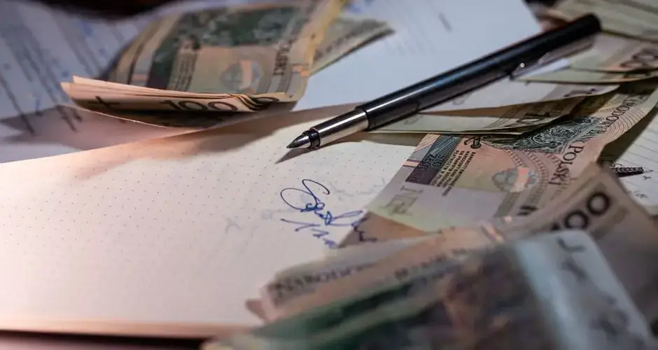 Overhead view of Polish banknotes, documents, and a pen on a desk, highlighting financial planning.