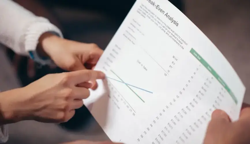 Close-up of hands discussing a break-even analysis document in a business meeting.
