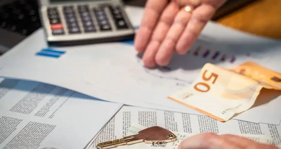 Hands examining financial documents, a 50 euro note, and a key, suggesting investment or real estate themes.