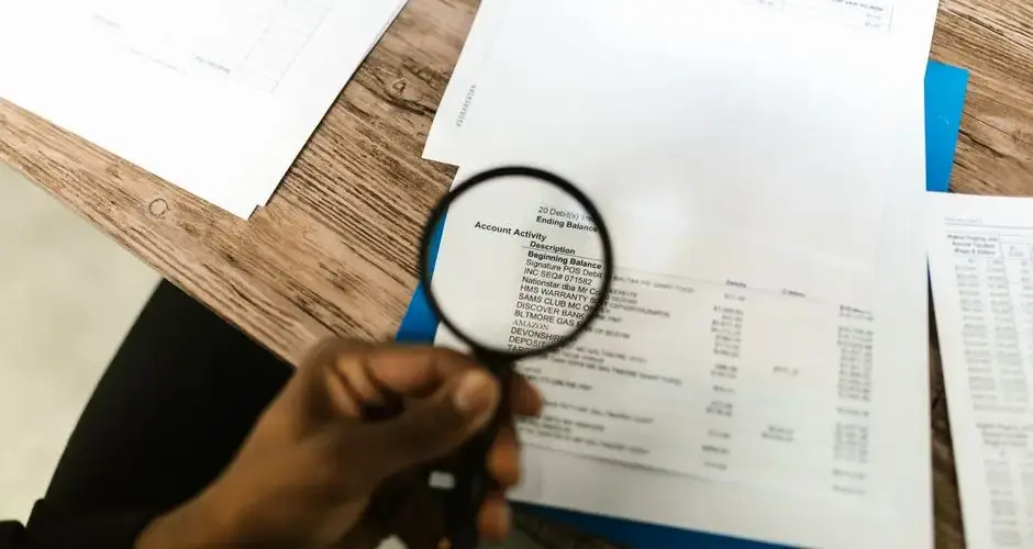 Close-up of hand using magnifying glass to review documents. Ideal for financial themes.
