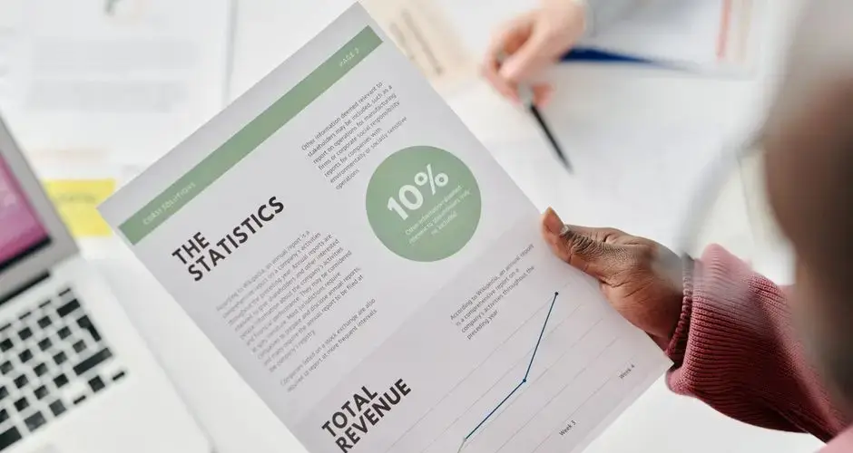 Hands holding a statistical report during a business meeting. Includes revenue graphs and analysis.