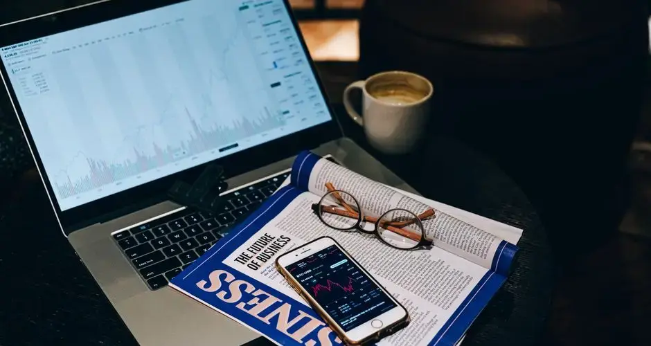A professional workspace featuring a laptop, smartphone, coffee cup, and business magazine on a table.