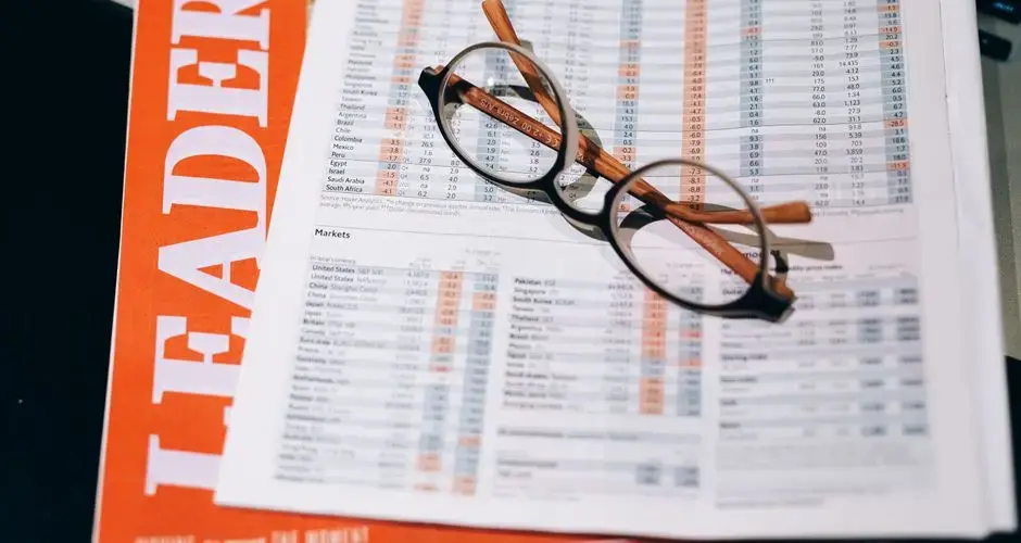 A pair of eyeglasses resting on a financial document and magazine with bold headline "LEADERS" in focus.