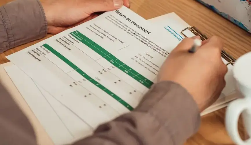A person analyzing a return on investment report with a pen in hand on a desk.