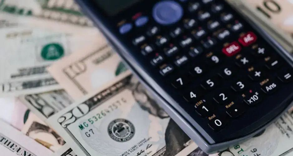 From above of electronic calculator placed over American cash paper money for budget planning and income and expenses calculation