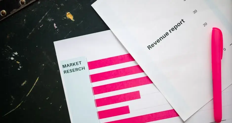 Close-up of market research charts and a revenue report with a pink pen on a desk.
