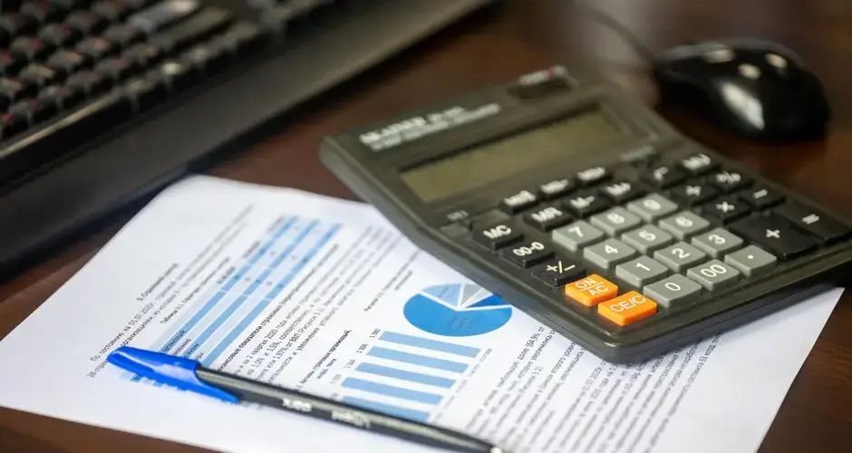 Desk with calculator, financial report, and pen, suggesting business analysis.