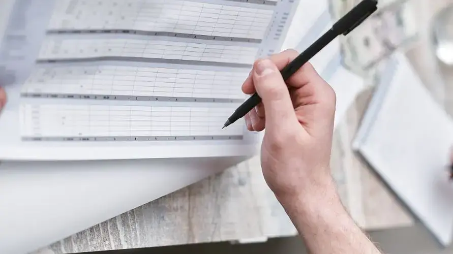 A close-up of a person holding a pen reviewing a financial document with cash visible, ideal for business themes.