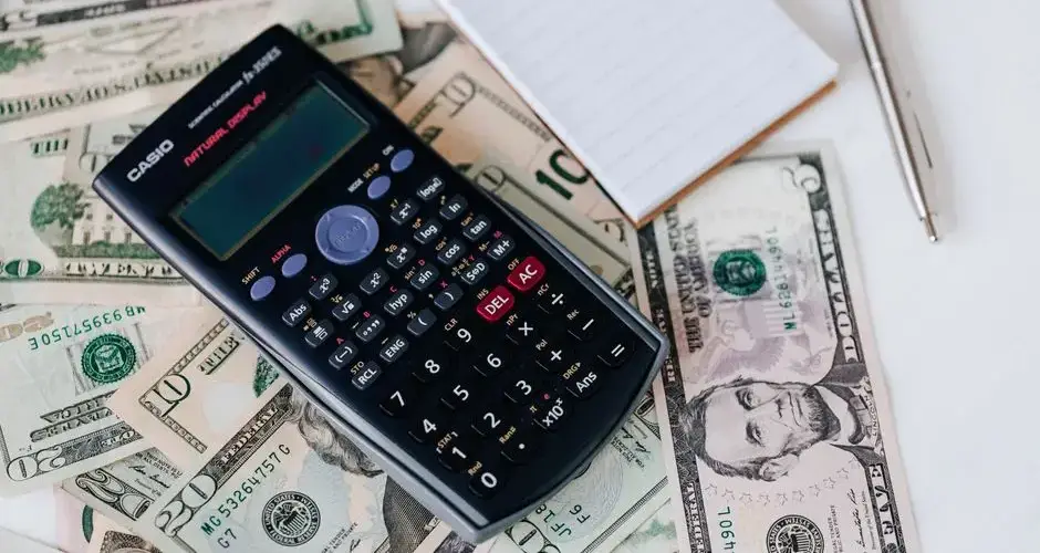 From above electronic calculator and notepad placed over United States dollar bills together with metallic pen for budget planning and calculation