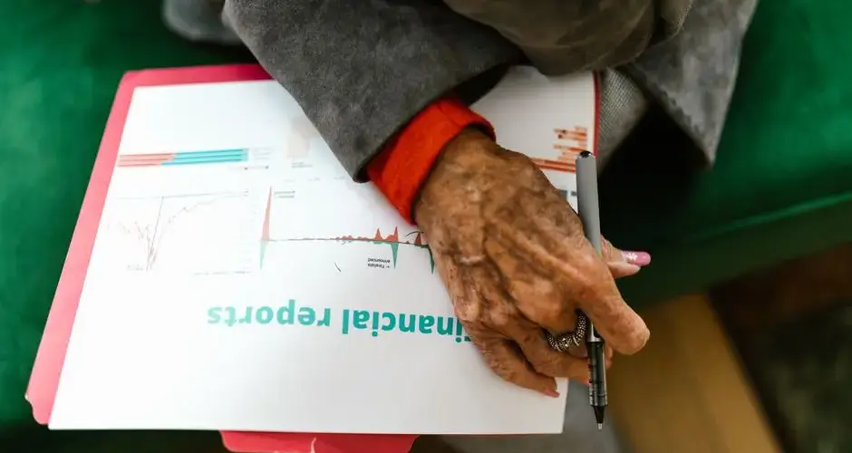 Close-up of an elderly woman holding a pen with a financial report.